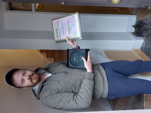 A photograph of Aaron Belcher accepting his Most Inspirational Garden trophy and certificate