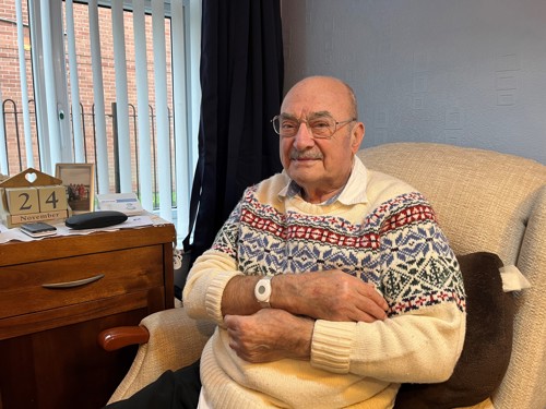 A photograph of Bill Watmore sat in his chair showing his Nottingham on Call wrist pendant